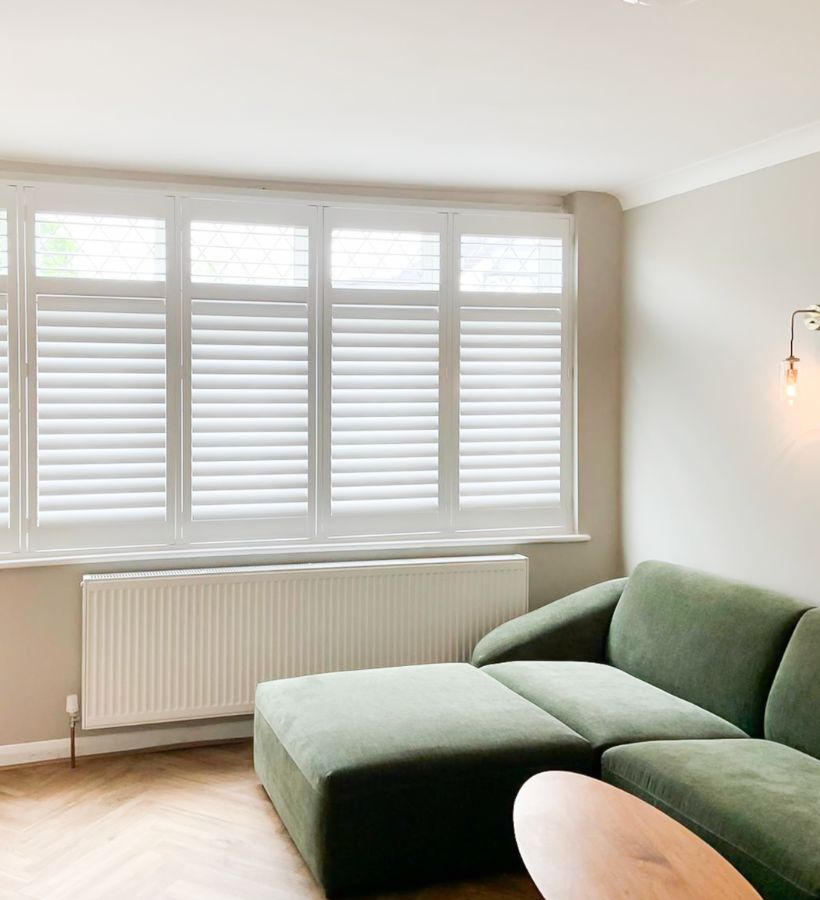 Living room with green sofa and white window shutters
