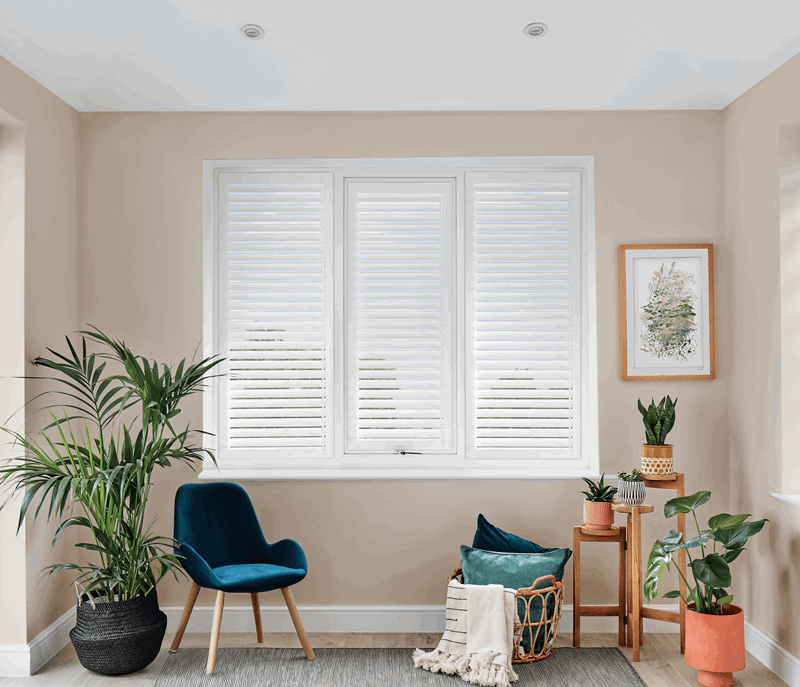 Living room with white shutters, plants, and a blue chair.