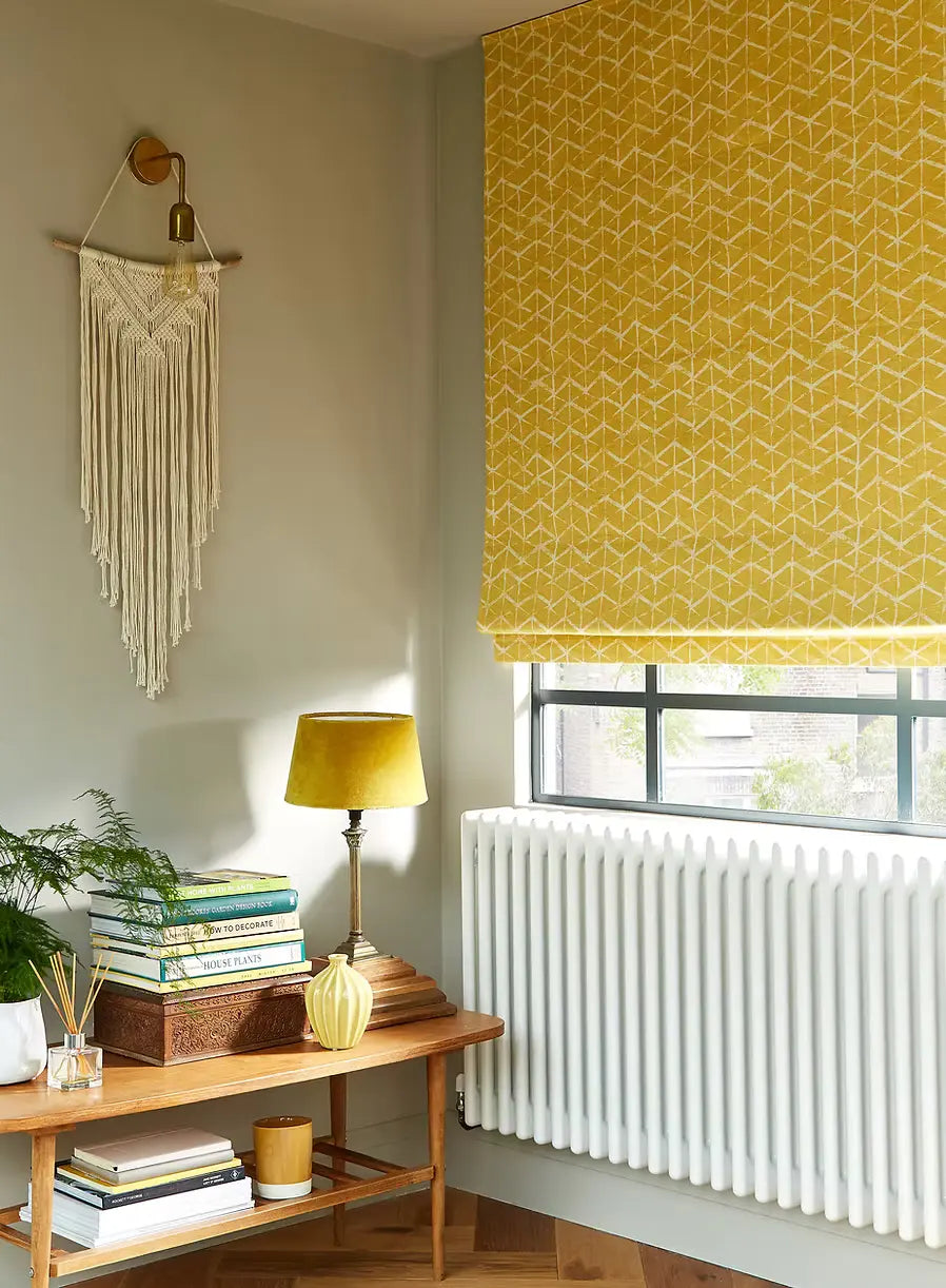 Living room with yellow geometric blinds, wooden shelf, and macrame wall hanging.